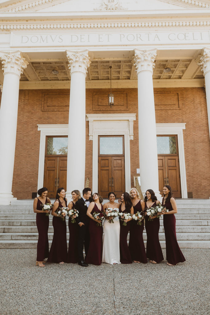 Bride and her bridal party laugh together in front of the St. Aloysius Church before the wedding ceremony begins.
