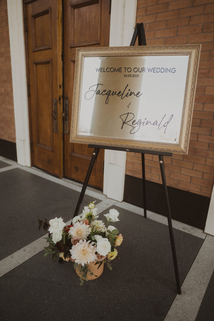 Name sign on a mirror with a floral arrangement stands in front of the entrance to the church.