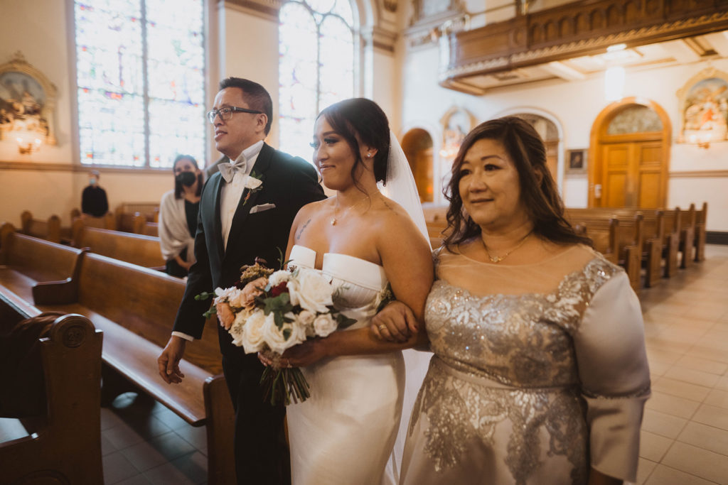 Bride walks down the aisle at the St. Aloysius church with her mother and father.