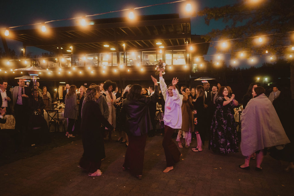 Bridesmaid celebrates after catching the bridal bouquet under the romantic cafe string lights at Beacon Hill