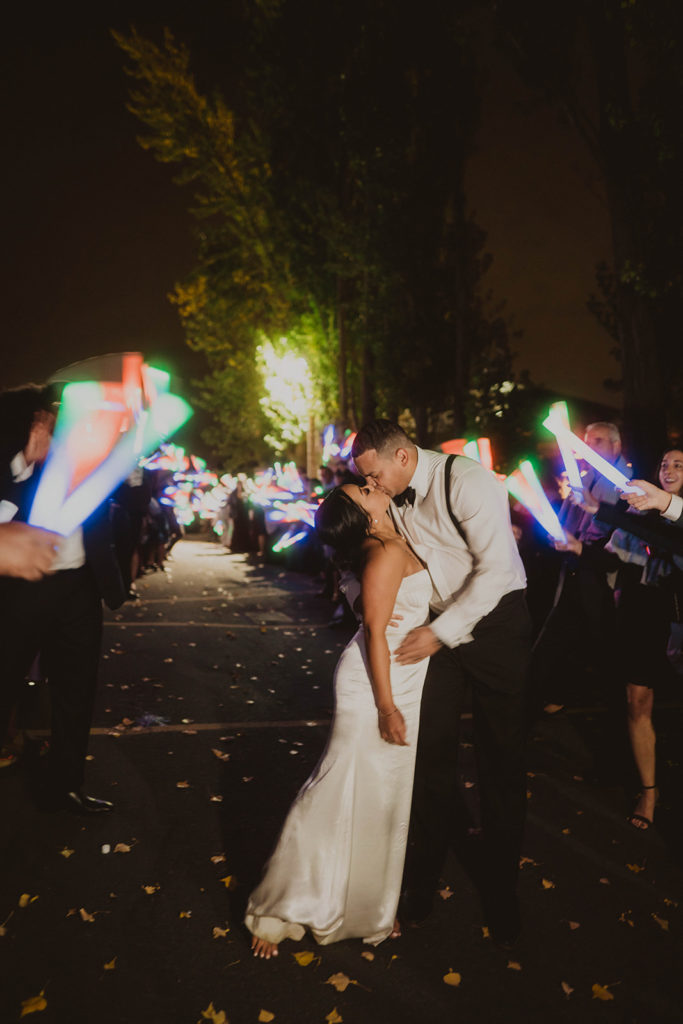 Newlyweds kiss amidst the glowing wands during their wedding reception exit after their wedding at Beacon Hill