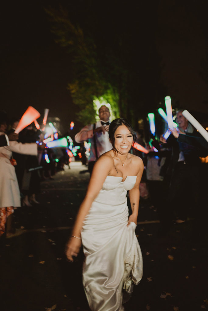Bride laughs as she runs down through the glowing wand exit with her groom behind her after their wedding at Beacon Hill