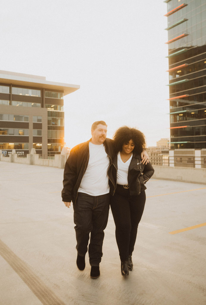 couple smiles as they walk on a parking garage at sunset 