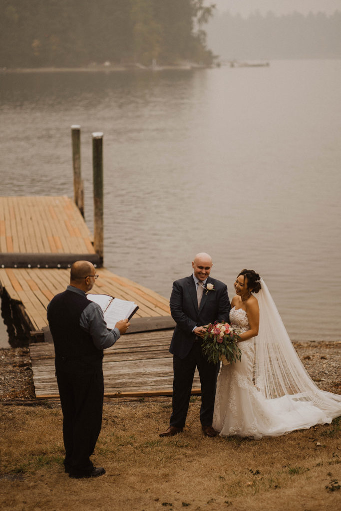 bride and groom smile during their lakeside Tacoma elopement ceremony as the elopement officiant speaks