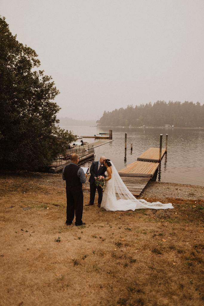 bride and groom laugh together with American Lake in the background during their lakeside Tacoma elopement