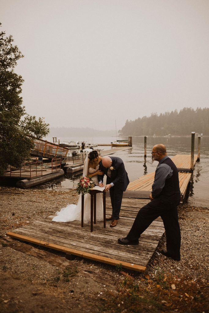bride and groom sign their marriage certificate on the dock of American lake