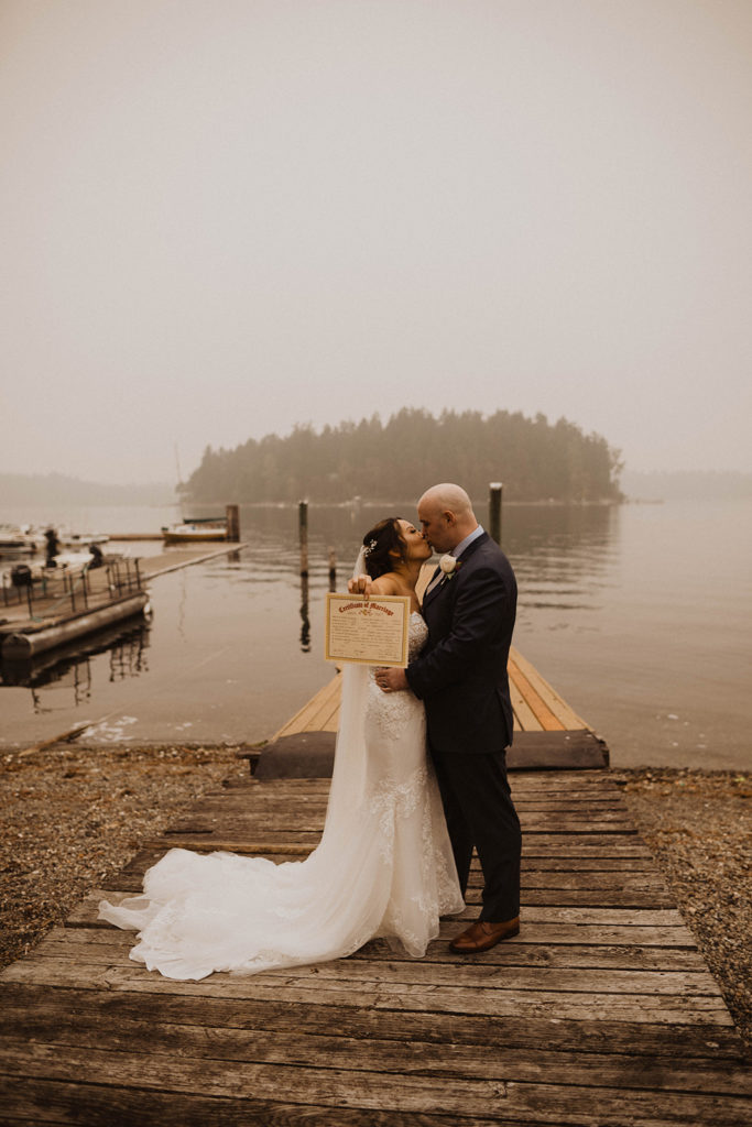 bride and groom kiss while holding their marriage certificate after their Tacoma elopement