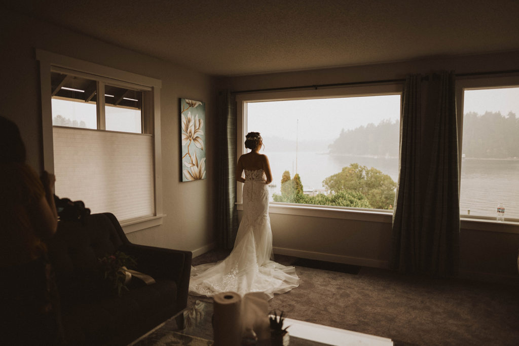bride looks out the window at the picturesque Tacoma lake before her elopement ceremony begins