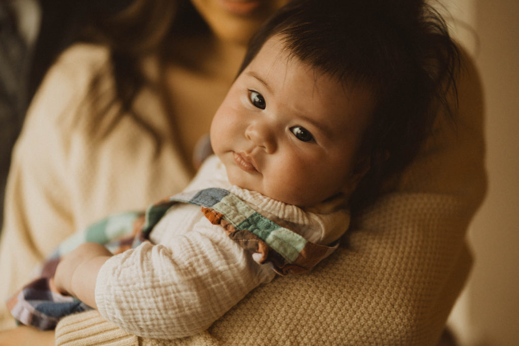 baby looks at the camera as her mom holds her in her arms during their seattle family lifestyle session