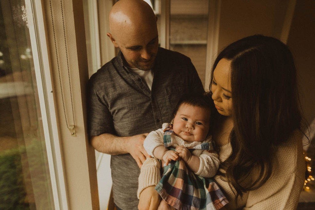 family stands beside the window during their in home Seattle family lifestyle session