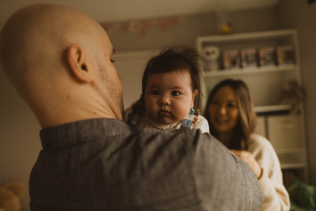baby makes a face in her nursery as her dad holds her during their family session