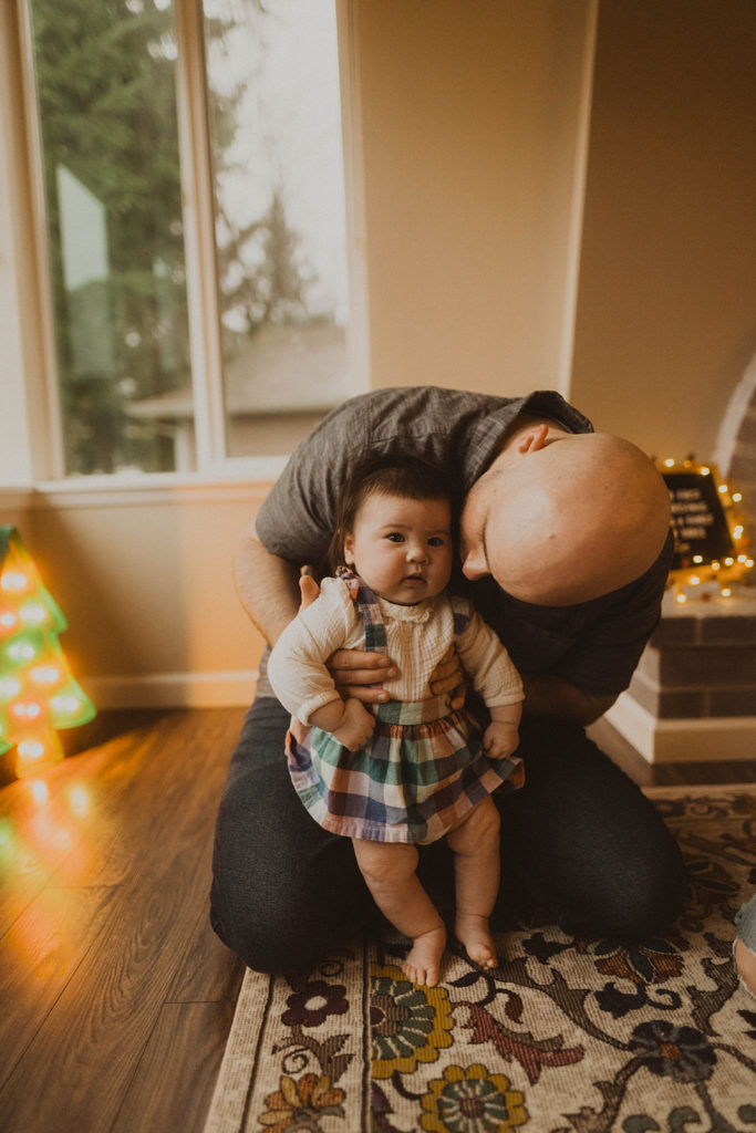 baby being held by her father as she stands on the rug in the living room