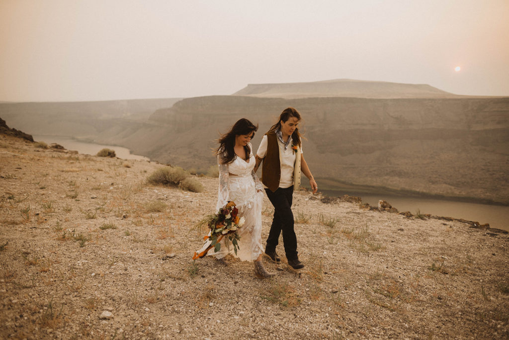 brides walk together on the rim of the snake river canyon during their elopement