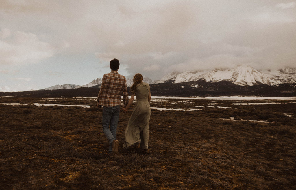 couple holds hands and walks toward the mountains in stanley during their engagement session