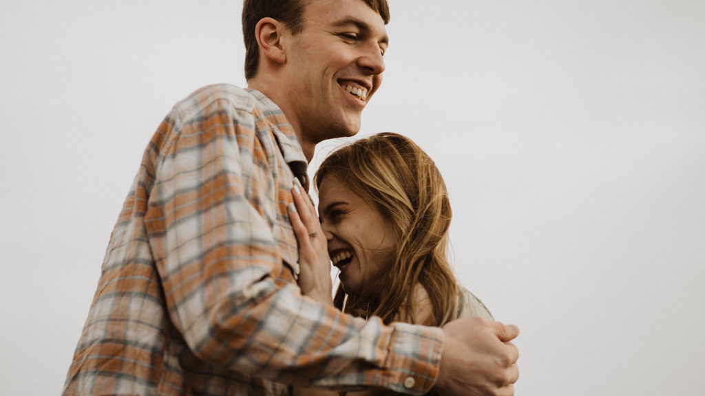 couple laughs together in the wind during their engagement session in the Sawtooth mountains